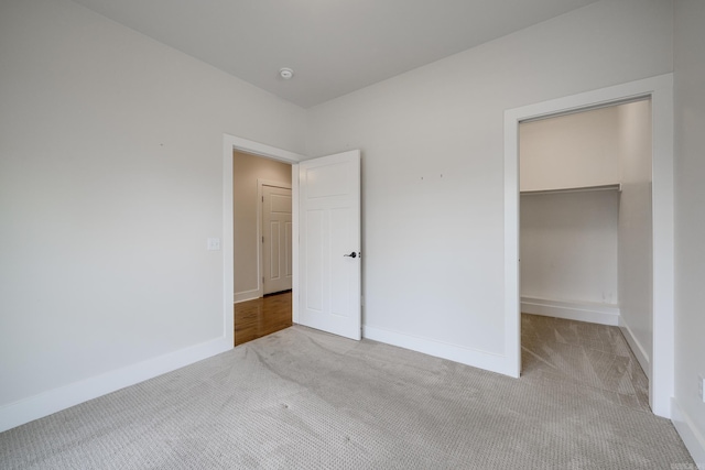 unfurnished bedroom with baseboards, a walk in closet, carpet, and a closet