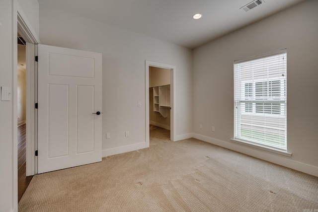 unfurnished bedroom with visible vents, light carpet, a walk in closet, and multiple windows