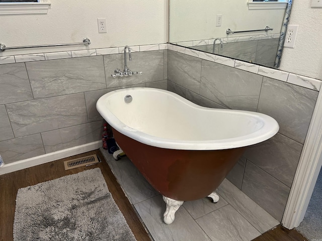 full bath with visible vents, a freestanding bath, wood finished floors, and tile walls