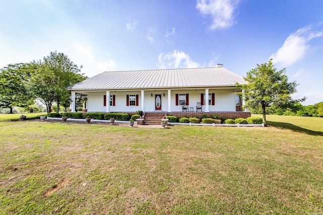 country-style home with covered porch, brick siding, metal roof, and a front yard