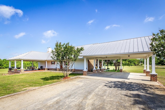 view of front of property featuring a front yard, a chimney, a carport, driveway, and metal roof