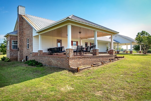 back of property featuring a standing seam roof, a chimney, metal roof, brick siding, and a yard
