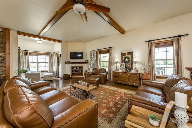 living area with ceiling fan, a glass covered fireplace, lofted ceiling with beams, and wood finished floors