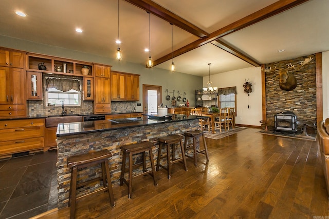 kitchen featuring brown cabinetry, a wood stove, a chandelier, tasteful backsplash, and a sink