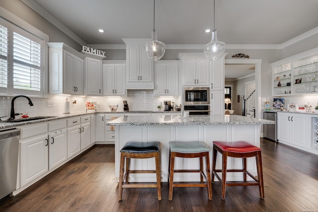 kitchen with a sink, a kitchen breakfast bar, stainless steel appliances, white cabinetry, and ornamental molding