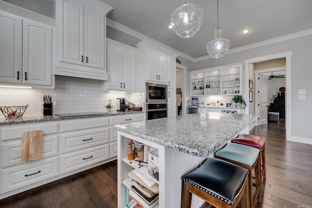 kitchen featuring open shelves, light stone countertops, a center island, ornamental molding, and black appliances
