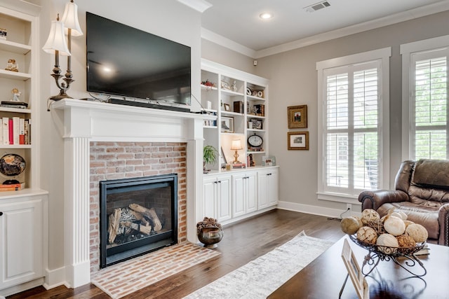 living room featuring visible vents, crown molding, a brick fireplace, dark wood finished floors, and built in shelves