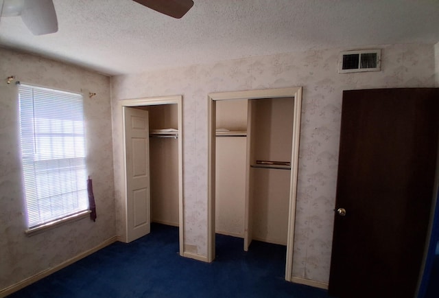 unfurnished bedroom with carpet flooring, ceiling fan, a textured ceiling, multiple closets, and visible vents