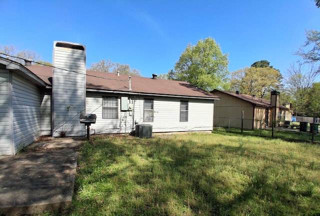 back of property featuring a lawn, fence, a chimney, and central AC unit