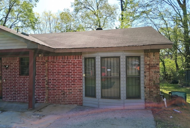 view of home's exterior with brick siding, a patio area, and roof with shingles