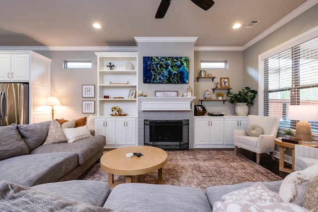 living room with visible vents, ornamental molding, wood finished floors, a fireplace, and a ceiling fan