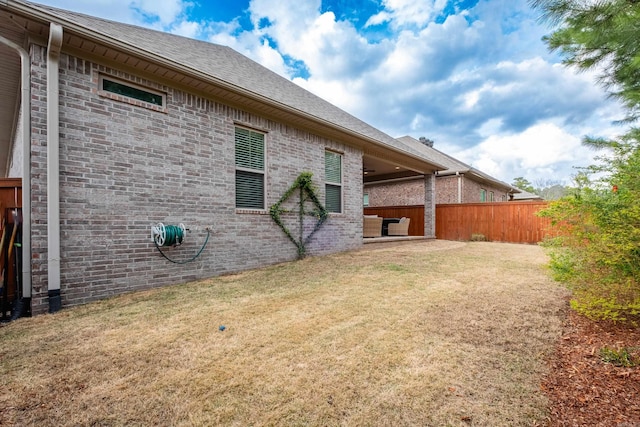 back of property with a yard, brick siding, fence, and roof with shingles