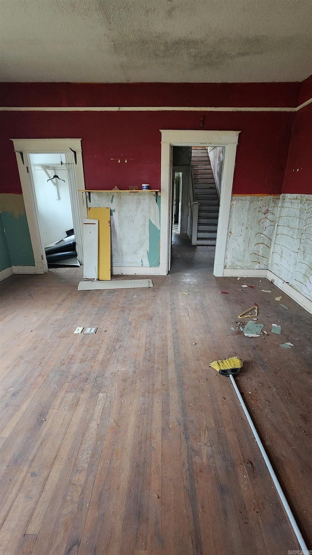 unfurnished living room with stairway, baseboards, a textured ceiling, and hardwood / wood-style floors