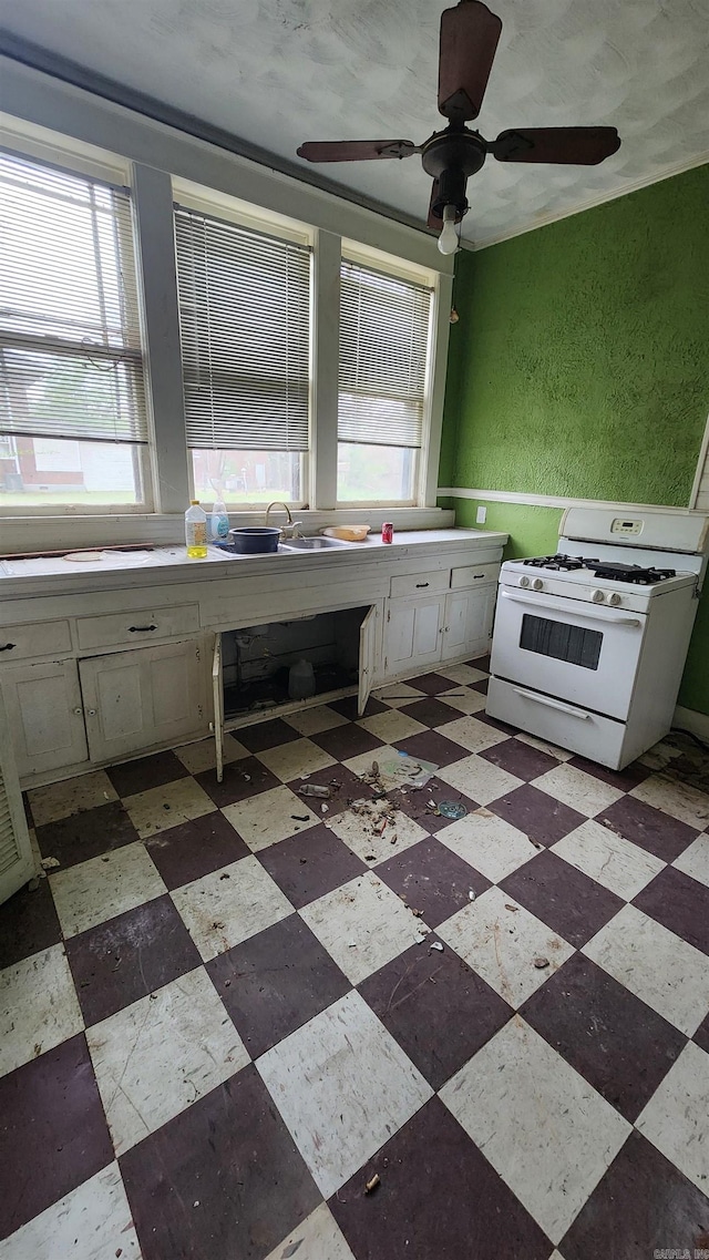 kitchen featuring white cabinets, a ceiling fan, white gas stove, and a sink