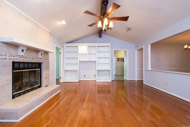 unfurnished living room featuring a fireplace, a textured ceiling, built in shelves, wood finished floors, and vaulted ceiling
