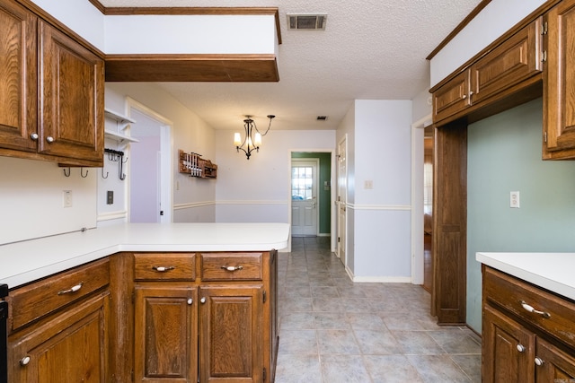 kitchen with brown cabinetry, visible vents, light countertops, a peninsula, and an inviting chandelier