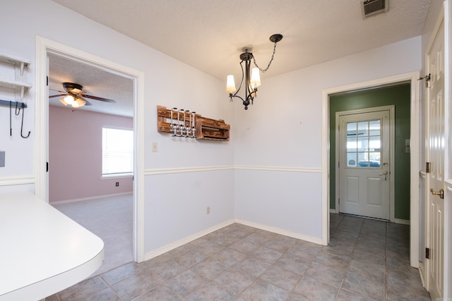 unfurnished dining area with a textured ceiling, baseboards, visible vents, and ceiling fan with notable chandelier