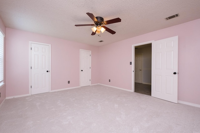 unfurnished bedroom with a ceiling fan, a textured ceiling, visible vents, baseboards, and carpet
