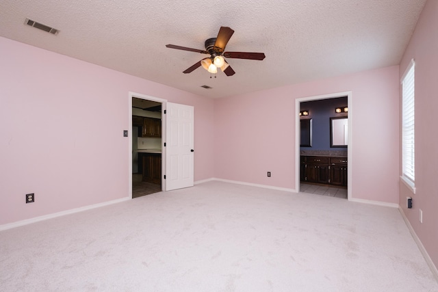 unfurnished bedroom featuring multiple windows, light carpet, ensuite bath, and visible vents