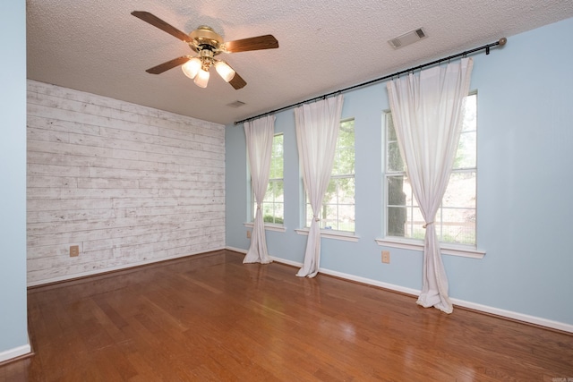 unfurnished room with a textured ceiling, a ceiling fan, baseboards, wood finished floors, and visible vents