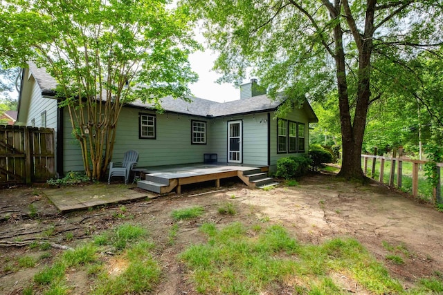 back of property with fence, a wooden deck, and a chimney