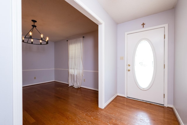 entryway with baseboards, wood finished floors, and a notable chandelier