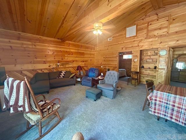 carpeted living area featuring visible vents, wood walls, ceiling fan, wooden ceiling, and lofted ceiling with beams