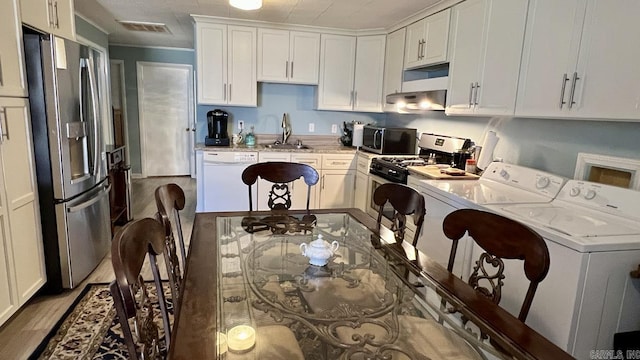 kitchen with a sink, stainless steel appliances, under cabinet range hood, visible vents, and washer and clothes dryer