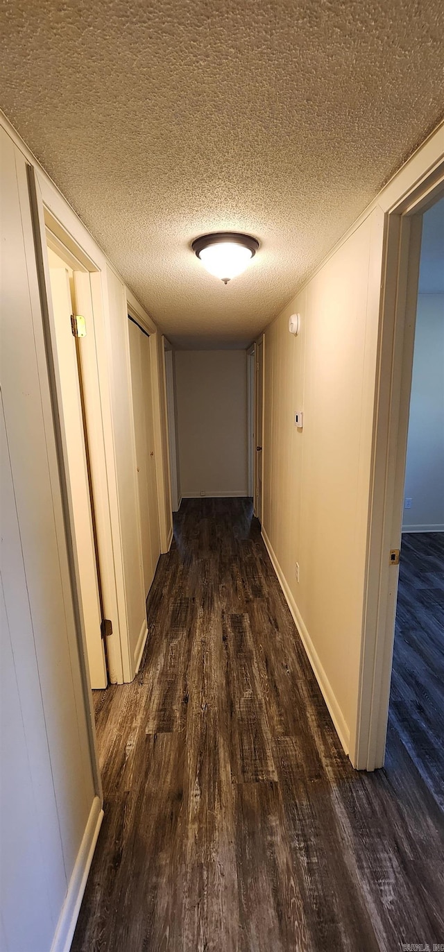 corridor featuring baseboards, a textured ceiling, and wood finished floors