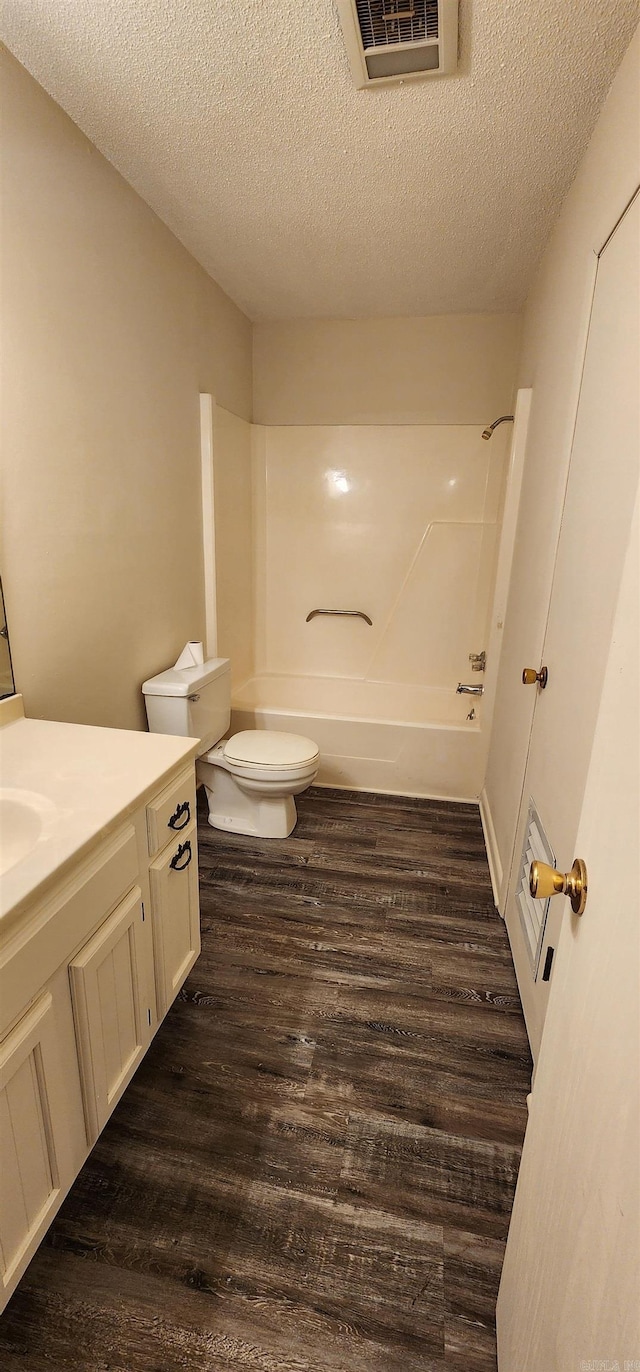 bathroom with vanity, toilet, a textured ceiling, wood finished floors, and visible vents