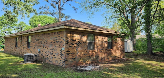 view of side of property featuring brick siding, central AC, and a yard