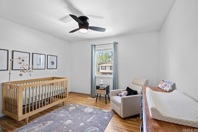 bedroom with ceiling fan, wood finished floors, and a nursery area