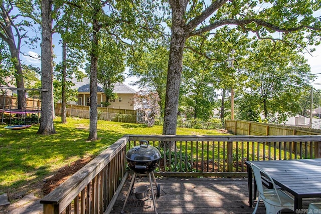 wooden terrace featuring a lawn, grilling area, a fenced backyard, and a trampoline