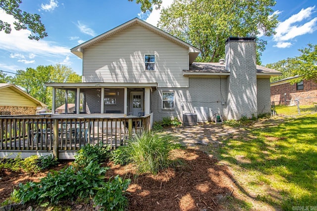 back of property featuring brick siding, a wooden deck, a chimney, cooling unit, and a lawn