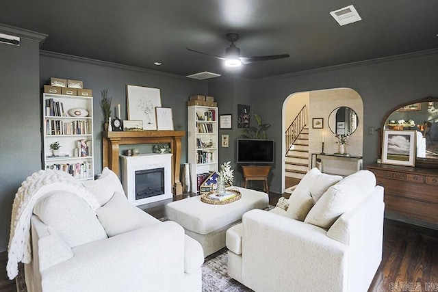 living area featuring a ceiling fan, crown molding, wood finished floors, stairway, and a glass covered fireplace