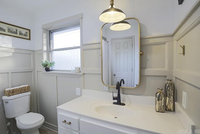 full bath with vanity, a decorative wall, and toilet