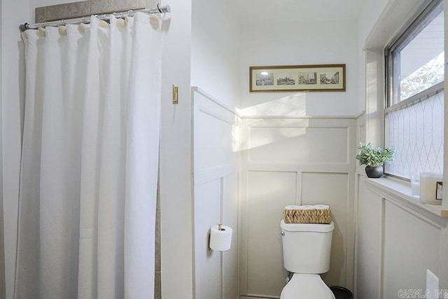 bathroom featuring toilet, a shower with curtain, a wainscoted wall, and a decorative wall