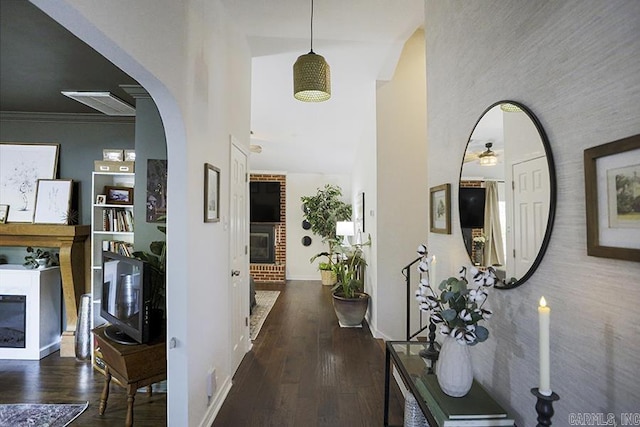hall featuring arched walkways, baseboards, wood finished floors, and a towering ceiling