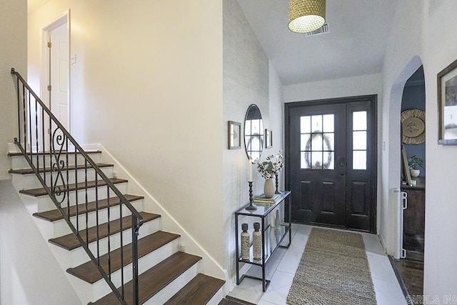 tiled entrance foyer featuring stairs, arched walkways, and visible vents