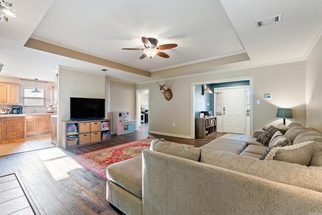 living room with crown molding, a ceiling fan, light wood-type flooring, a tray ceiling, and visible vents