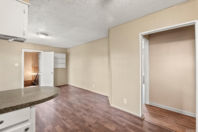 unfurnished living room with baseboards, dark wood-style flooring, and a textured ceiling
