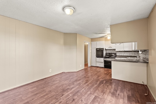 kitchen featuring dark countertops, decorative backsplash, black appliances, and dark wood-type flooring
