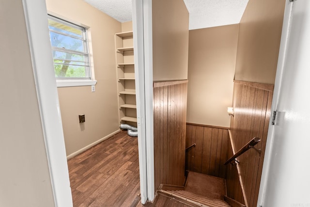 staircase featuring a textured ceiling, wainscoting, wood finished floors, and wood walls