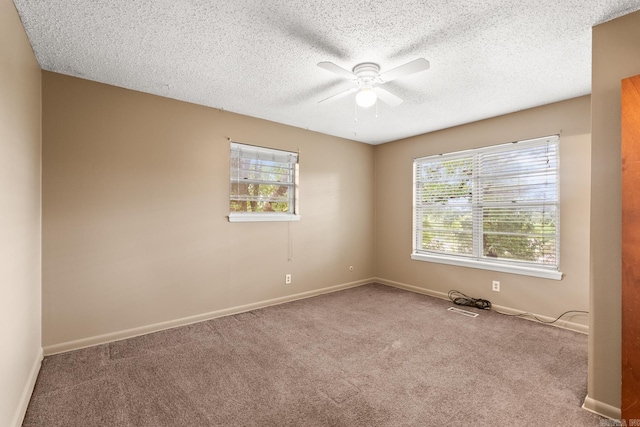 carpeted empty room with a textured ceiling, ceiling fan, visible vents, and baseboards