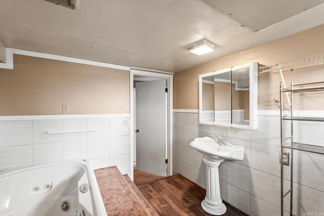 full bath featuring tile walls, wainscoting, a tub with jets, and visible vents