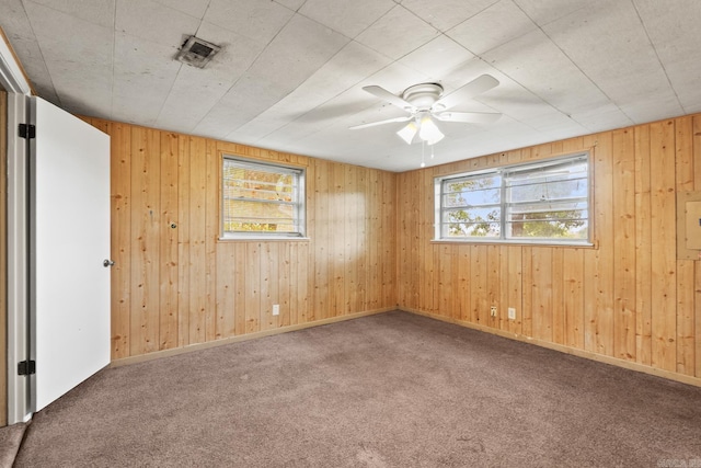 carpeted spare room with wooden walls, a ceiling fan, and visible vents