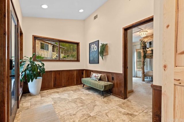 living area featuring stone finish floor, visible vents, wainscoting, wood walls, and recessed lighting