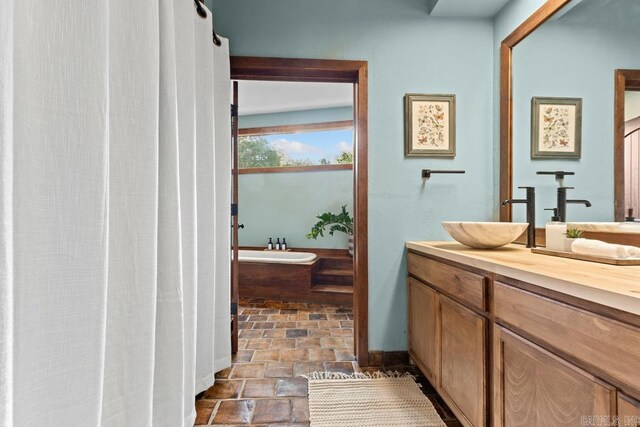 full bath featuring a bathtub, stone finish floor, and vanity