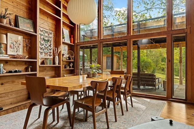 dining room with plenty of natural light, wood walls, wood finished floors, and a towering ceiling