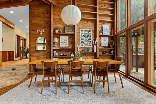 dining area featuring wood finished floors, high vaulted ceiling, beamed ceiling, wooden walls, and recessed lighting